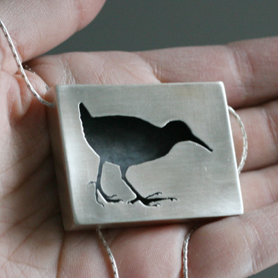 Luhtakana-kaulakoru. Koruun on tämän jälkeen vaihdettu ketjusysteemi. Nyt korun sivuilla on kaksi lenkkiä, joihin voi kiinnittää nahkanauhan tai papuketjun.